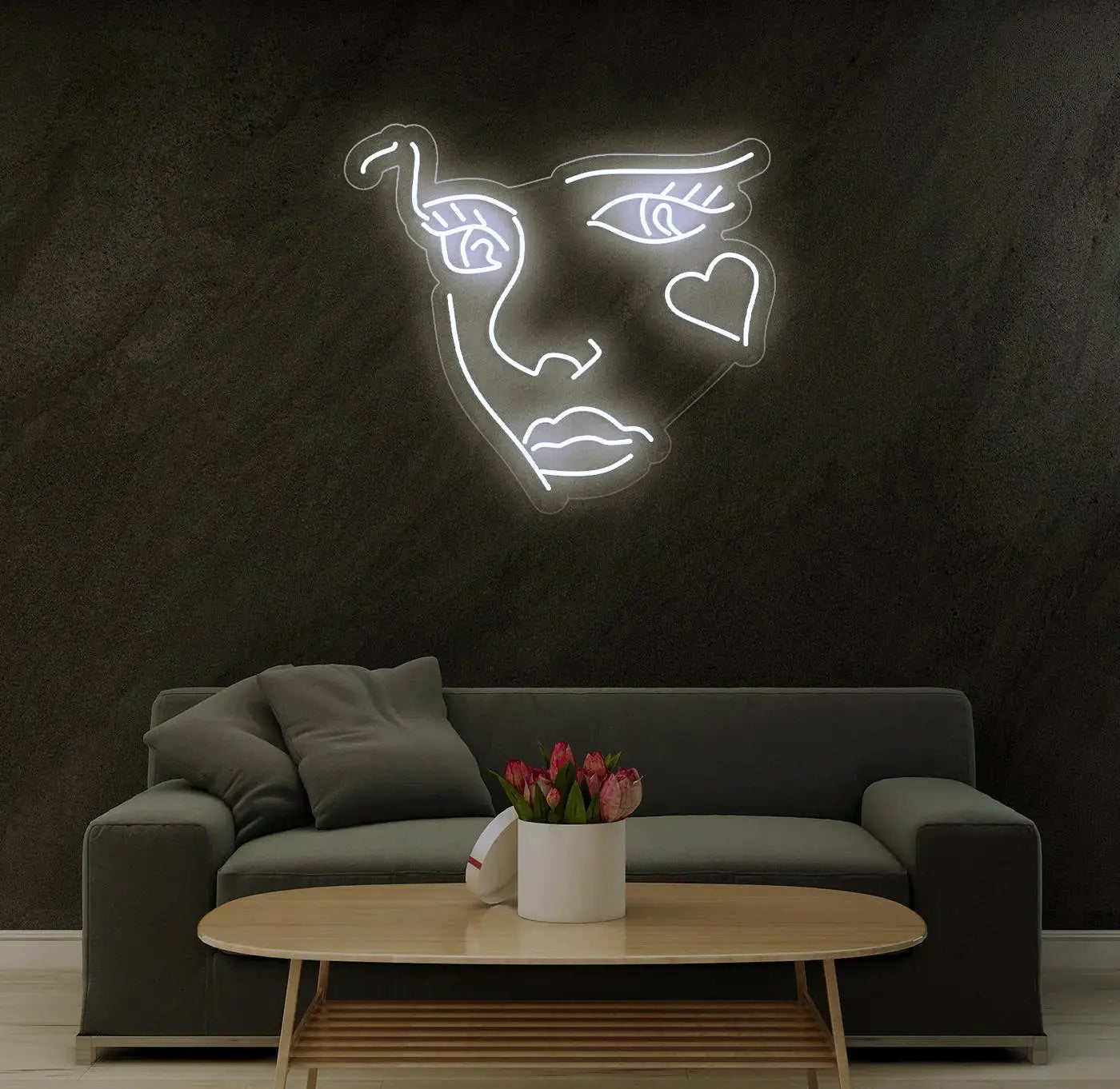 Néon LED visage abstrait blanc fixé sur un mur sombre au dessus d’un canapé et d’une table basse modernes.