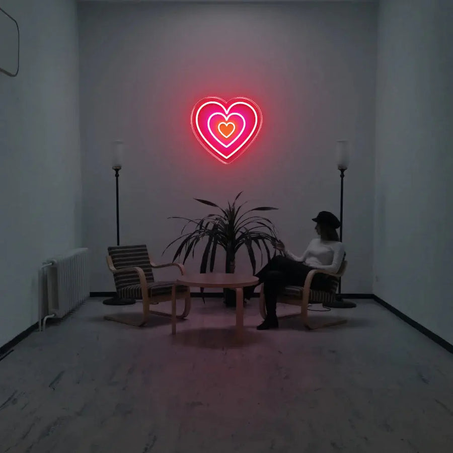 Néon mural en forme de cœur superposé aux tons rouge, rose et orange, installé au-dessus d’un espace lounge minimaliste.