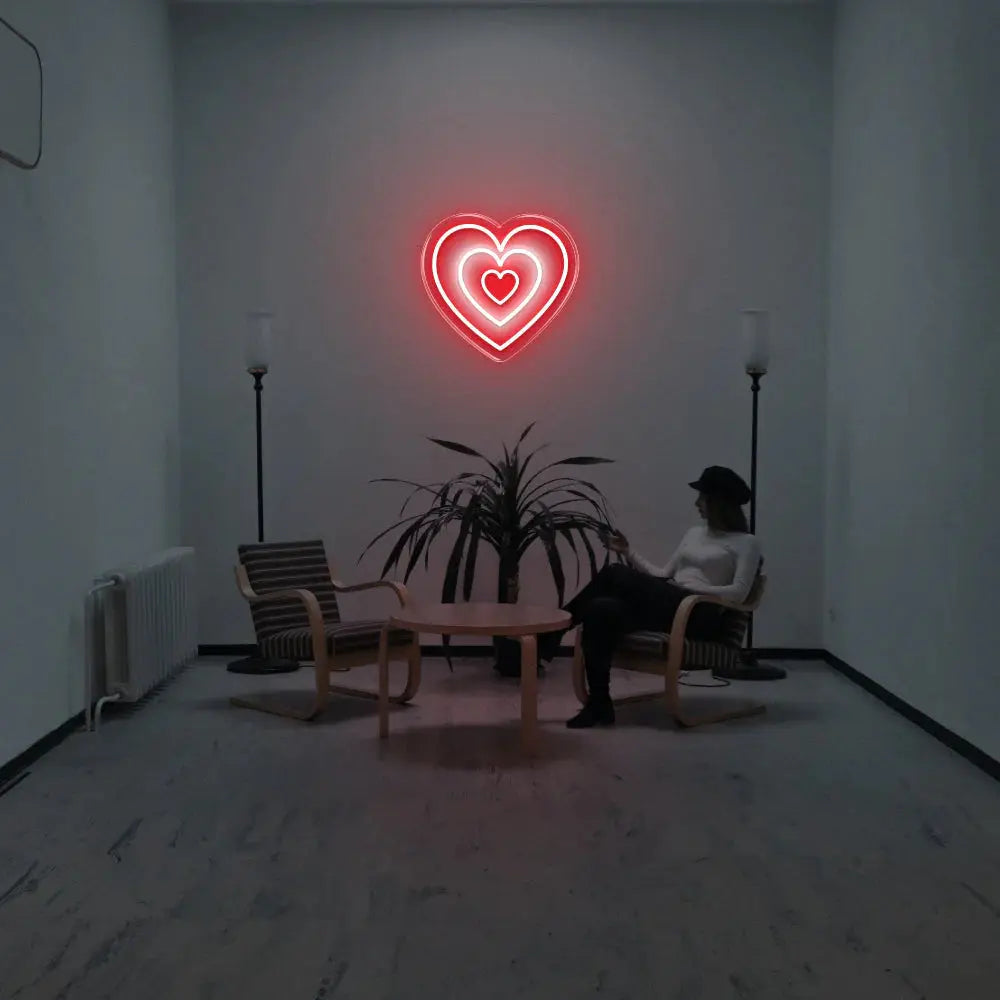 Néon mural en forme de cœur rouge éclairant une pièce moderne minimaliste avec fauteuils et plante centrale.