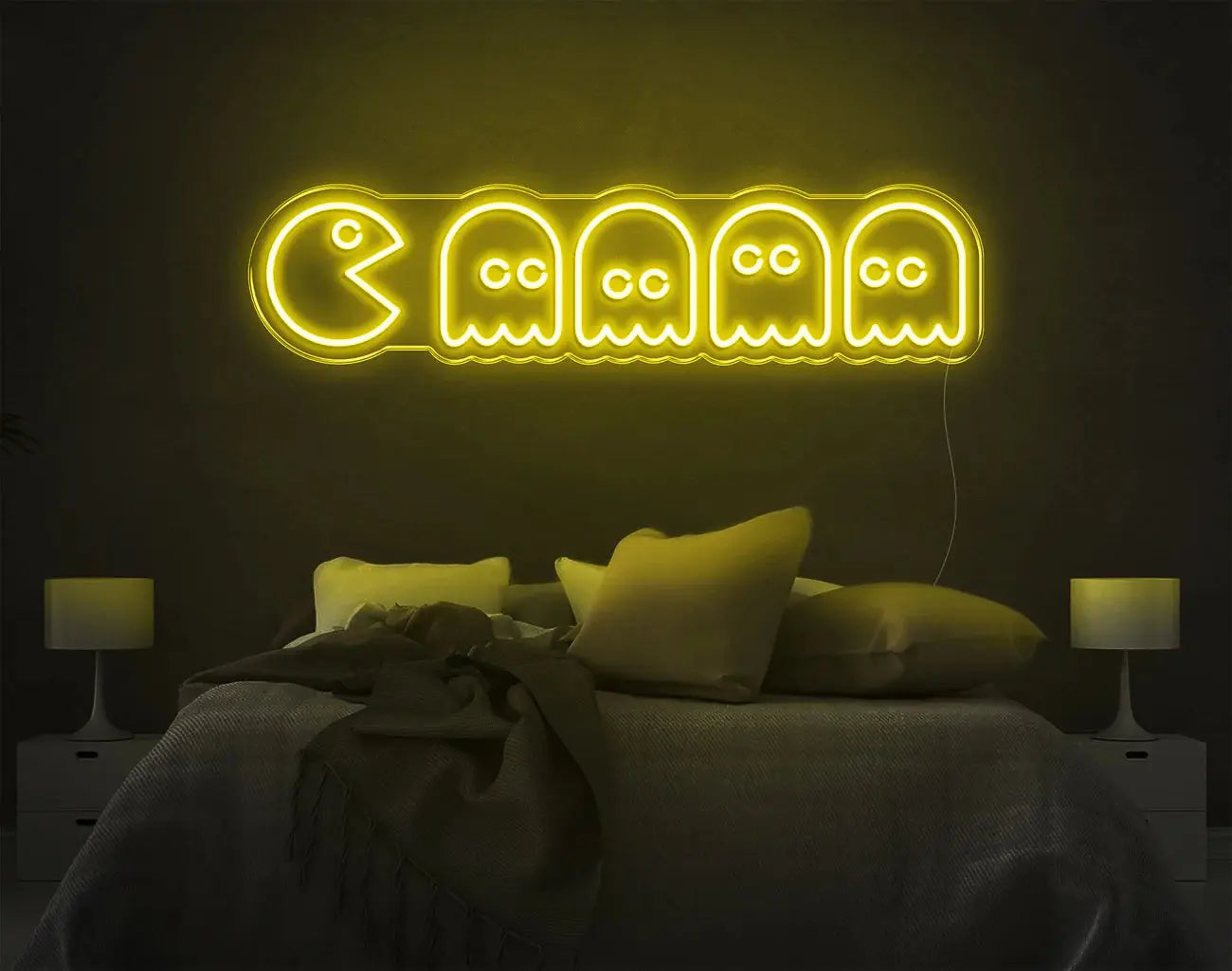 Enseigne LED néon Pacman jaune lumineuse au-dessus d’un lit pour une décoration rétro nostalgique.
