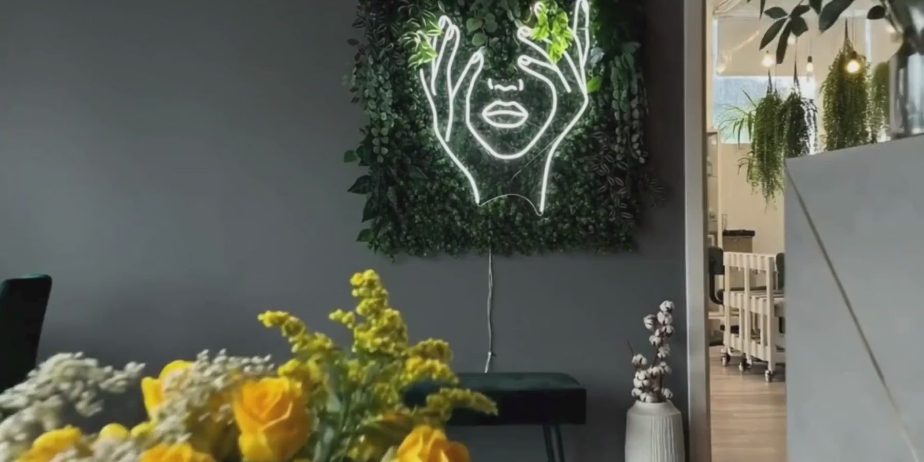 Enseigne néon LED visage abstrait blanc installée sur mur végétal dans un intérieur moderne