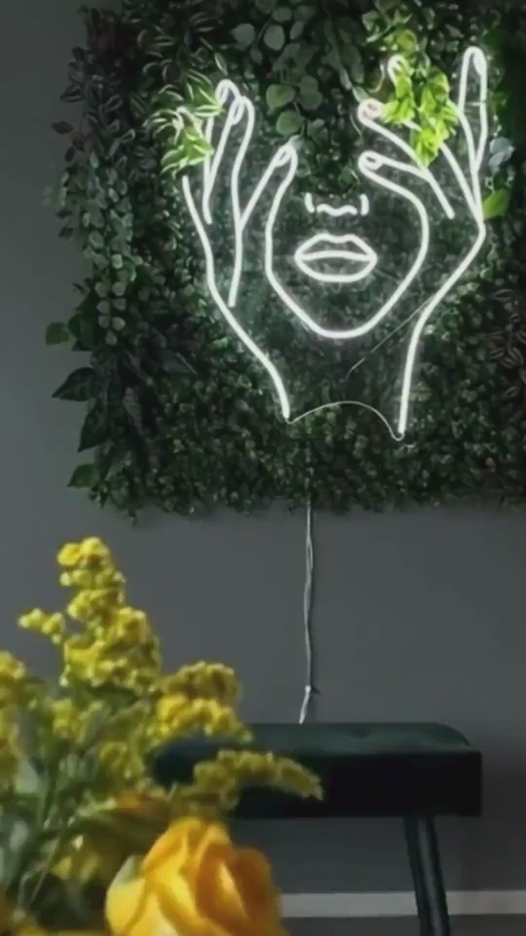 Enseigne néon LED visage abstrait blanc installée sur mur végétal dans un intérieur moderne.